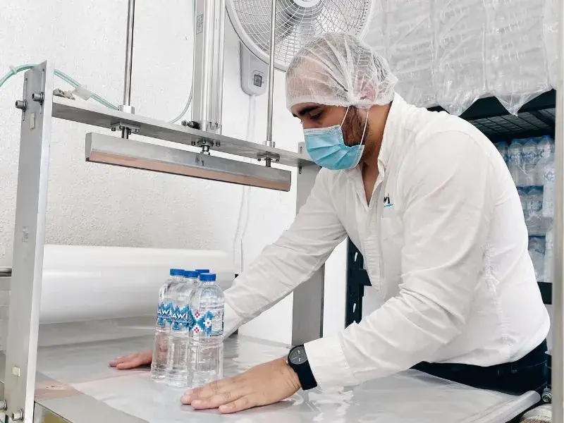 Colaborador de Bawi con cofia y cubrebocas sellando botellas de agua purificada